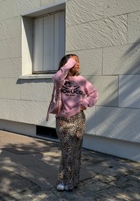 Suéter rosa claro con gráfico negro, combinado con una falda larga de leopardo. Los accesorios incluyen un bolso transparente y zapatos plateados brillantes.