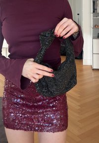 Borsa nera con perline e manico superiore annodato, che mostra una varietà di perline scintillanti su una superficie liscia. Indossata con una gonna di paillettes color borgogna.