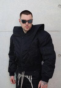Veste bomber noire avec un col surdimensionné, des poches zippées et des poignets côtelés, associée à un pantalon noir avec des accents de texte blancs.