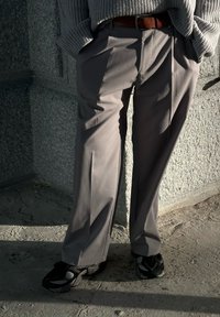 Pantalon gris à jambes larges en tissu lisse, avec une taille plate et des poches latérales, associé à des baskets noires et grises.