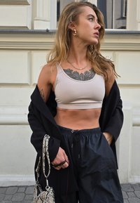 Bežasti kratki top, crne široke hlače i crni kaput. Dodaci uključuju torbu sa motivima i zlatne naušnice. Čista koža sa vidljivim tetovažama.