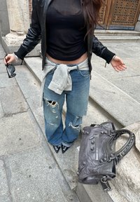 Črni kratki top, usnjena bomber jakna, denim širokih hlač z obrabljeno teksturo, siva karo srajca zavezana okoli pasu, črni koničasti čevlji z visoko peto, siva torbica.