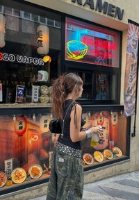 Ramen trgovina z neonskimi napisi in dekorativnimi lampioni. Jedilniki so prikazani v steklenem oknu, ki vsebujejo pisane krožnike, vzorčaste teksture in oznake.