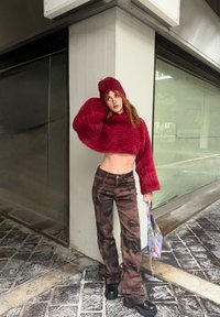 Pull court duveteux bordeaux et bonnet assorti, associés à un pantalon à motif camouflage. Bottes plateformes noires et sac multicolore complètent le look.