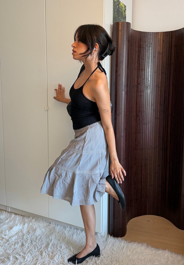 Femme en haut noir et jupe grise étire la jambe en arrière tout en équilibrant sur l'autre pied, tenant le talon de la chaussure et touchant une armoire blanche.