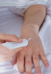 Vit tub av kräm med en spets, som appliceras på en hand. Hånden ligger på en ljus yta, med synlig hudstruktur och minimal hårväxt.