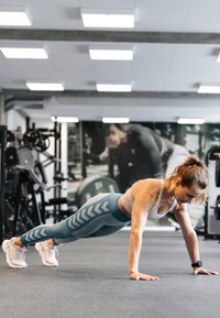Träningsoutfit med ljusgrå sportbh och turkosa leggings med chevronmönster, bärs under en armhävning i en gymmiljö.