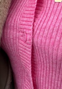 Strak zittend roze geribd vest met een knoopsluiting, gemaakt van zacht gebreid materiaal, met een subtiele textuur en een verticaal streeppatroon.