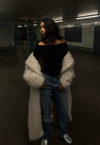 Hvit faux pelsjakke, svart off-shoulder topp, blå jeans og sølv sneakers. Den teksturerte jakken kontrasterer med glatte stoffer og denim.