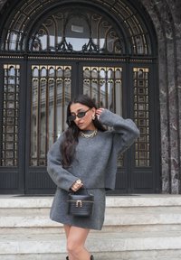 Szürke kötött pulóver és miniszoknya szett, texturált anyagb�ól, kis fekete krokodilmintás táskával, aranyozott fémrészletekkel és díszítésekkel párosítva.