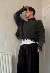 Pull gris court avec accents côtelés, coupe ample, ourlet  à franges, superposé à un haut blanc, associé à un pantalon large à carreaux noirs.