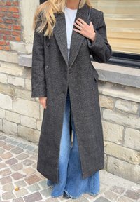 Mørkgrå hørfanguldsjakke med dobbeltknaplukning, store klapper og sidelommer, båret over brede jeans i blå.