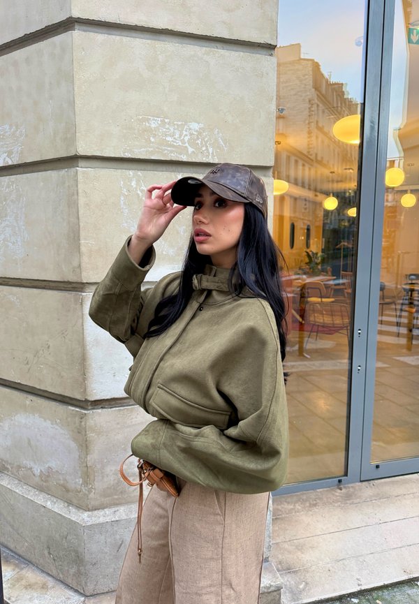 Olivengrøn cropped jakke med høj krave og forlommer, kombineret med en brun læderkasket. Neutrale beige bukser med vidde i benene.