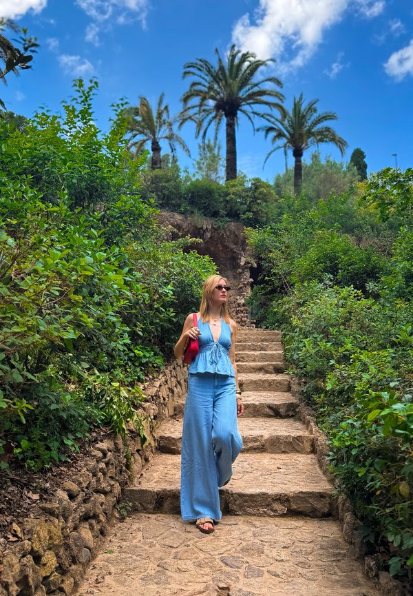 Femme en tenue bleue descendant des marches en pierre entourée de verdure avec des palmiers et un ciel bleu au-dessus.