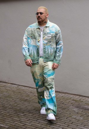 Chaqueta y pantalones de mezclilla en colores pastel con estampados de naturaleza, con un ajuste relajado y patrones distintos de árboles y nubes. Zapatillas blancas puestas.