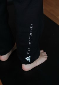 Zwarte joggingbroek met elastische boorden, voorzien van witte tekst "STELL/MC CARTNEY" op de zijkant en een Adidas-logo nabij de zoom.