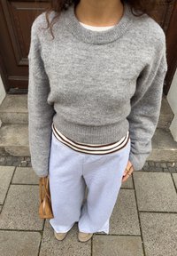 Grå strikket sweater med rund hals, kombineret med lysegrå vidde-sweatpants med en brun- og hvidstribet talje.
