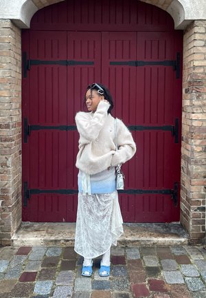 Light beige, fuzzy sweater layered over a blue gradient top. A white lace skirt drapes over light trousers, paired with blue open-toed shoes.