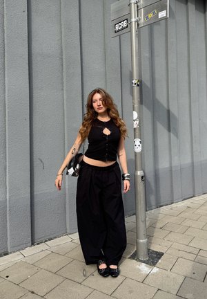 Top negro corto con detalle de botones, pantalones anchos de tiro alto negros y zapatos negros. Los accesorios incluyen una pulsera y un bolso de plata.