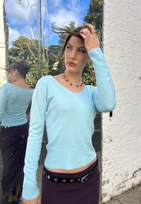 Lyseblå, tætsiddende V-hals sweater med lange ærmer og ribbestruktur, parret med en mørkelilla blyantnederdel og et metalbælte.