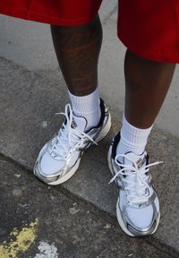 Hardloopschoenen met een witte mesh bovenkant, zilveren accenten en zwarte details. Draagt witte crew sokken, weergegeven op een gestructureerde stoep.