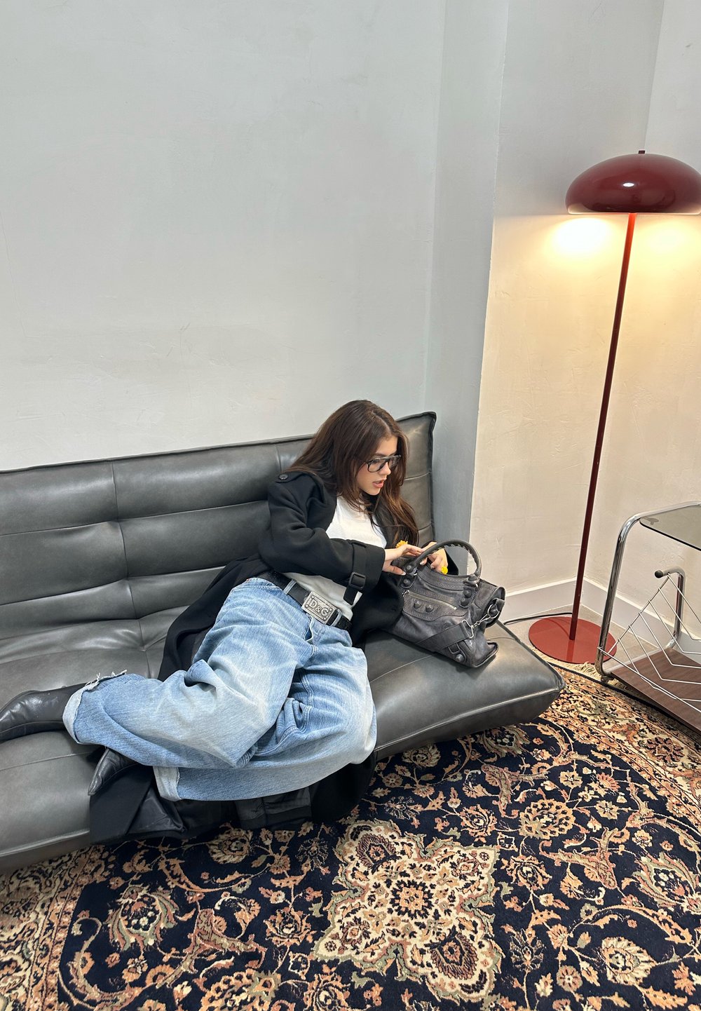 Črna usnjena zofa z vbodnim vzorcem in sivo denim priložnostno obleko. Vključuje sivo torbico, vzorčasto preprogo in moderno svetilko.