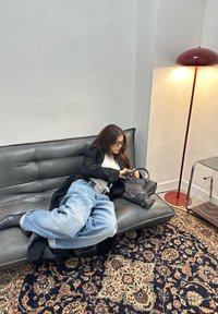 Črna usnjena zofa z vbodnim vzorcem in sivo denim priložnostno obleko. Vključuje sivo torbico, vzorčasto preprogo in moderno svetilko.