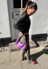 Purpursoma soma ar mezgatu rokturi, gluda tekstūra, apvienota ar olīvu zaļām biksēm un sarkaniem sporta apaviem. Redzama melna īsa ādas jakas.