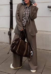 Costume brun surdimensionné avec pantalon à jambes larges, superposé avec une chemise à carreaux. Sac à main marron foncé avec des fermetures éclair, chaussures blanches à plateforme. Chapeau gris texturé.