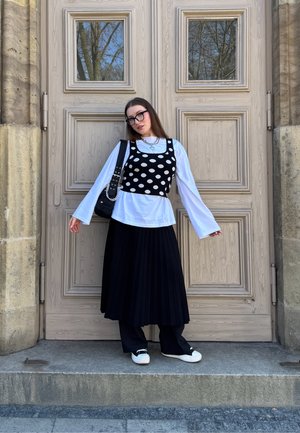 Top corto de lunares en blanco y negro sobre una camisa blanca de manga larga, combinado con una falda negra con pliegues y zapatillas negras. Bolso negro y accesorios.