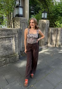 Leichtes Leopardenmuster-Body mit quadratischem Ausschnitt, dunkle weit geschnittene Hosen und bunte Tiermuster-Sneaker. Natürliche Umgebung im Hintergrund.