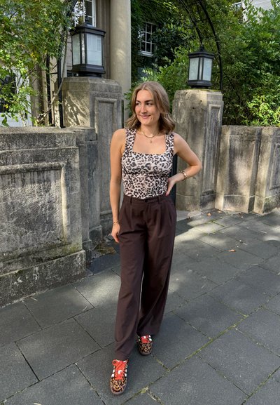 Bodis de leopardo ligero con escote cuadrado, pantalones de pierna ancha oscuros y zapatillas de deporte con estampado animal colorido. Entorno natural al fondo.