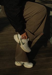 Vita sneakers med gröna accenter, texturerad mesh-ovandel, tjock vit sula, bärs med khaki-byxor i en solbelyst utomhusmiljö.