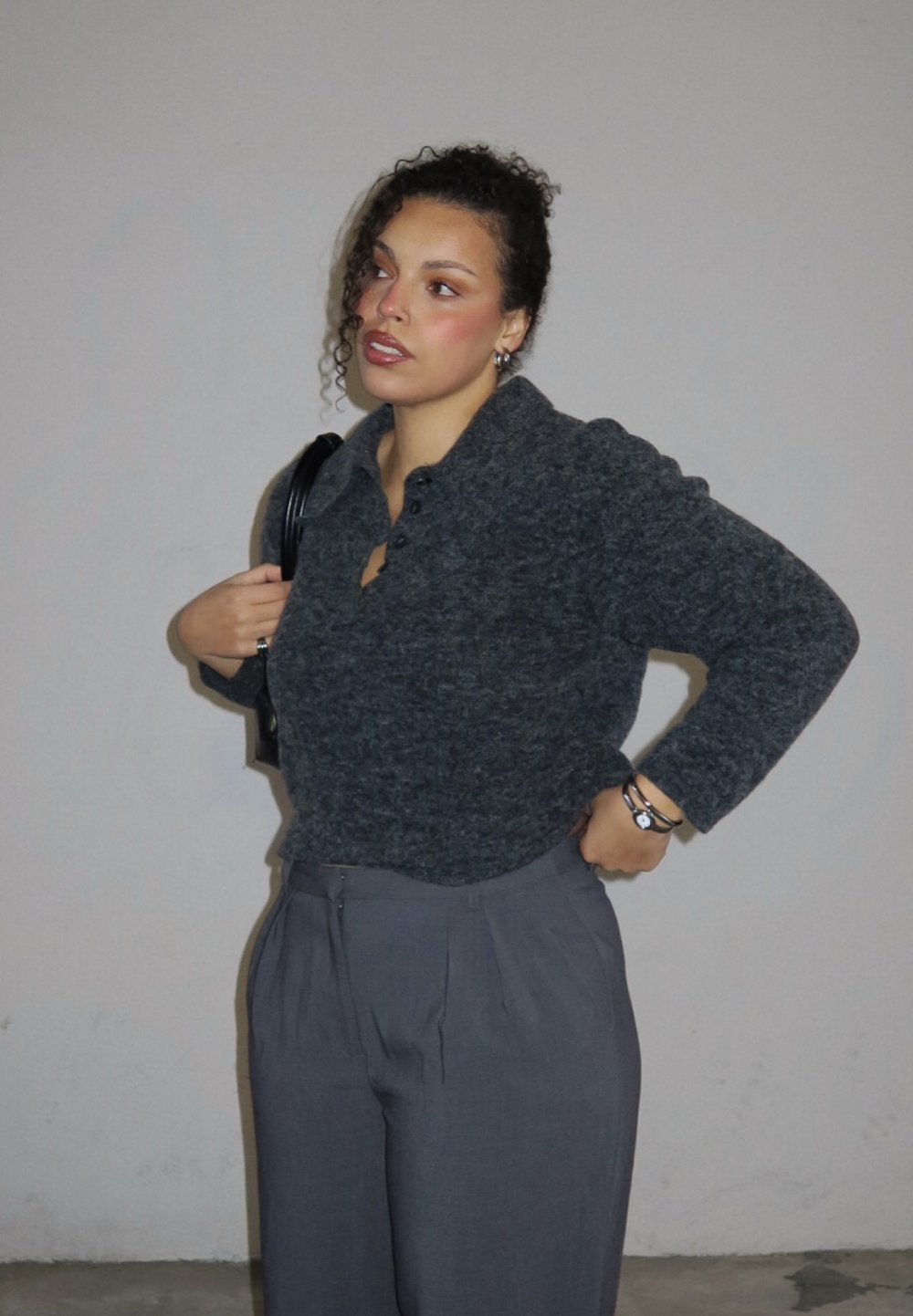 Houtskoolgrijze, cropped wollen trui met een kraag en knopen, gecombineerd met hooggetailleerde grijze broek met plooien.