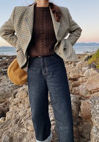 Dvojřadový houndstooth blazer v žluté, hnědé a černé; hnědý svetr s kabelovým pletením; vysoké tmavé džíny; kulatá hnědá taška.