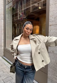 Chaqueta de dos botones beige claro con hombros pronunciados, llevada sobre una blusa blanca ajustada, combinada con jeans de pierna ancha azul oscuro y un bolso con estampado.