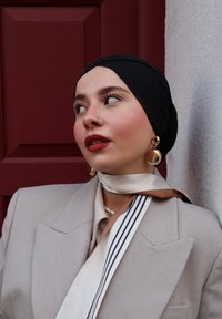 Blazer gris clair avec de larges revers, foulard noir et boucles d'oreilles en or. Foulard en soie crème avec des rayures sombres, sur un fond bordeaux.