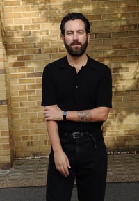 Μαύρο κοντομάνικο πόλο μπλουζάκι με υφασματική υφή, σε συνδυασμό με μαύρο παντελόνι με ψηλή μέση. Εντυπωσιακό τατουάζ στον αριστερό πρόβλημα, με ασημένια κοσμήματα που προσθέτουν έμφαση.