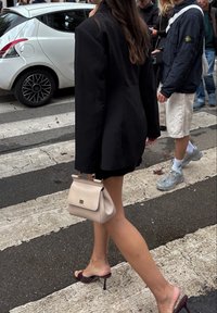 Črn oversize srajc, kratka črna krila, svetlo bež torba z zaponko, sijoče burgundske sandale s peto, hodi po prehodu.