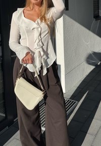 Blusa bianca a maniche lunghe con ruches e scollo a V, abbinata a pantaloni scuri a vita alta e una piccola borsa color crema.