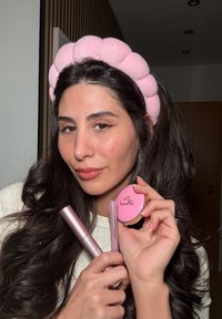 Roze, zachte haarband met ronde vormen; houdt een roze mascara, een lipproduct en een compact met "Sweet" erop gegraveerd; gladde texturen.