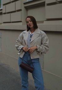 Jachetă bej scurtă cu guler larg, cămașă cu dungi, blugi albaștri cu talie înaltă și o mică geantă de umăr din fibră de bumbac în culoare burgundă. Texturi netede.