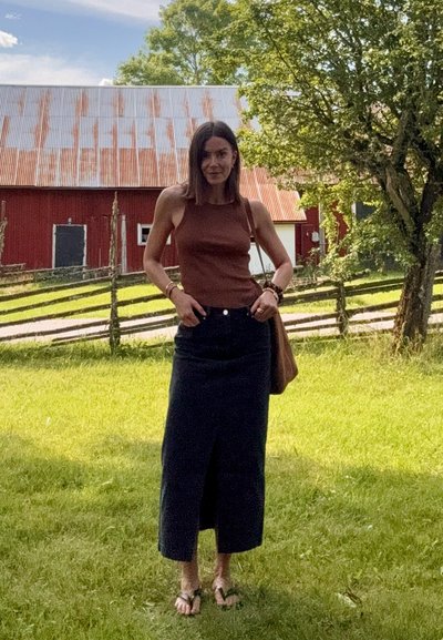 Top marrón sin mangas combinado con una falda maxi de mezclilla oscura, con una abertura media. Los accesorios incluyen un bolso de hombro marrón y sandalias simples.