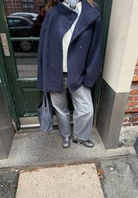 Temno modra mešana volnena obleka z visokim ovratnikom, lahki pulover, široke hlače z navpičnimi črtami, sive usnjene gležnjarice in siva torba tote.