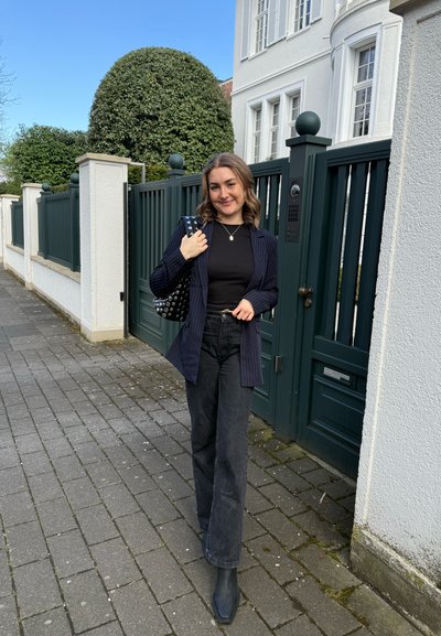 Blazer negro de rayas con un top negro, combinado con unos jeans negros de pierna ancha y botas de tobillo. Un bolso negro con tachuelas completa el conjunto.