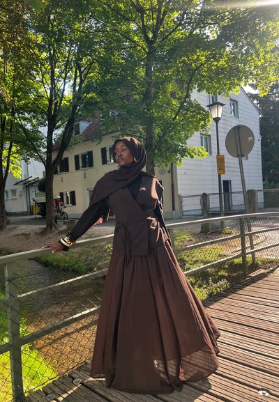 Conjunto marrón en capas con una parte superior ajustada y una falda fluida, hecho de tejido ligero. Un hijab a juego completa el look.