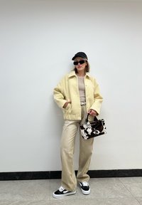 Κίτρινο φλις μπουφάν, μπεζ μπλούζα, μπεζ παντελόνι σε φαρδιά γραμμή, τσάντα με μοτίβο αγελάδας σε μαύρο και άσπρο, και μαύρα αθλητικά παπούτσια με λευκές σόλες. Μαύρο καπέλο, γυαλιά ηλίου.