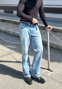 Black long-sleeve shirt, light blue relaxed fit jeans, and black leather ankle boots, standing next to a chain and post.
