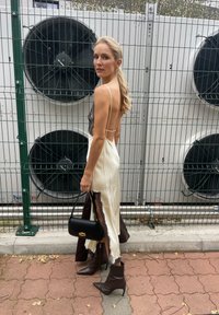 Off-white satijnen jurk met zwarte kantaccenten, rugloos ontwerp, hoge split, gecombineerd met bruine puntige enkellaarsjes en een kleine zwarte handtas.