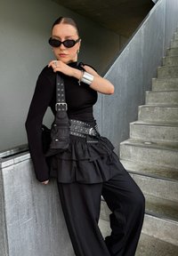 Μαύρη μπλούζα με μακριά μανίκια, στρωματοποιημένη μαύρη φούστα με ρυάκια, μαύρη ζώνη με ασημί καρφιά και μικρή μαύρη τσάντα χεριού. Συνδυάζεται με ασημί αξεσουάρ.